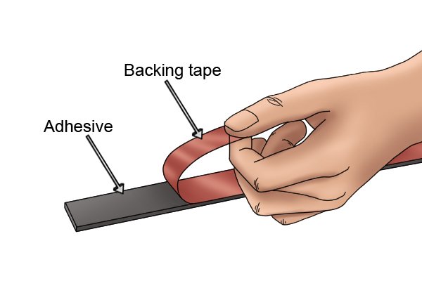 Peeling backing tape off flexible magnetic tape with labelled adhesive