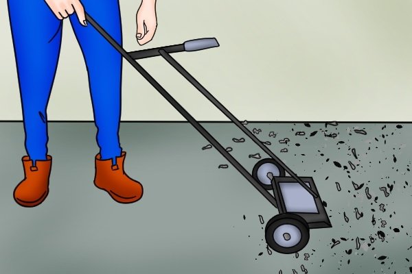Rolling a green heavy duty push magnetic sweeper along the ground over ferromagnetic materials