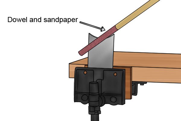 Use the vice and clamp the scraper with the concave curve facing up. Wrap the sandpaper around the dowel.     Run the dowel and sandpaper, forwards and backwards over the edge of the concave curve. Repeat this action until the edge of the scraper is smooth.