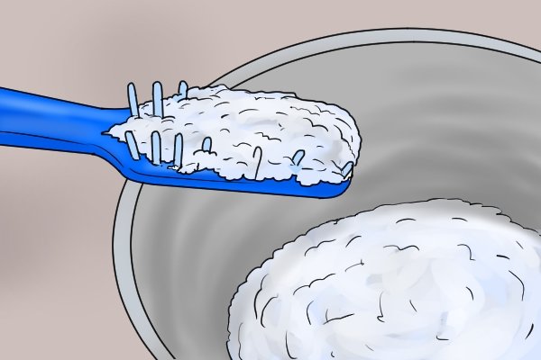 DIYer collecting grinding paste on a toothbrush so that it can be dabbed into the hole that was made with the guide screw