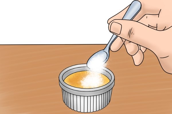 Sprinkling granulated sugar with a spoon onto the top of a creme brulee custard