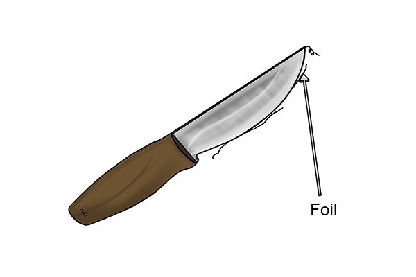 A DIYer removing the foil from the edge of their knife blade which has been created during the filing process