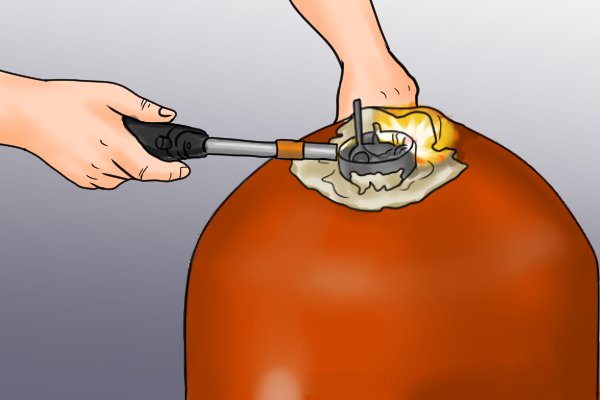 Image of a DIYer applying heat around the outsides of the immersion heater element with a blowtorch
