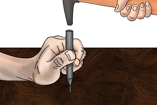 A black hammer with a rubber handle hitting a centre punch into a piece of wood