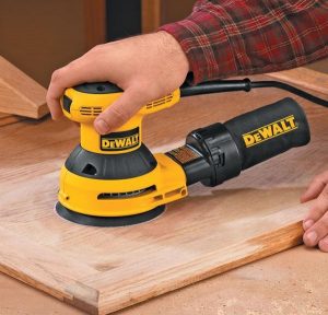 Individual using a DeWalt orbital sander on wood.