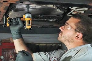 Individual using a DeWalt impact wrench on the bottom of a vehicle.